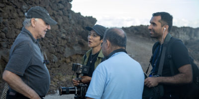 Four people standing in a circle on a rocky hill with camera equipment, smiling and talking to each other.