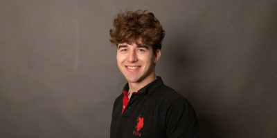 Image of a person on a dark grey background wearing a black shirt with a red logo.