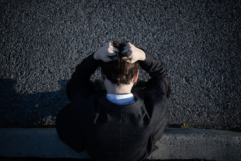 A birds eye view image of a person in a suit on the side of the sidewalk with their fists in their hair.