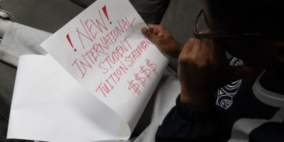 Student looks down at a long piece of paper that says, "NEW INTERNATIONAL STUDENT TUITION STATEMENT $$$$," with concern.