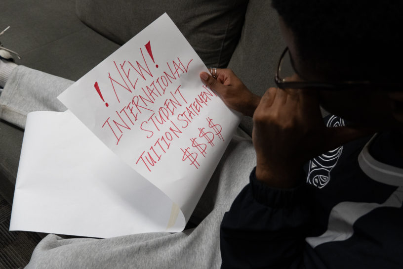 Student looks down at a long piece of paper that says, "NEW INTERNATIONAL STUDENT TUITION STATEMENT $$$$," with concern.