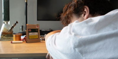 A person is laying their head on a desk looking at a package of THC and various other objects.