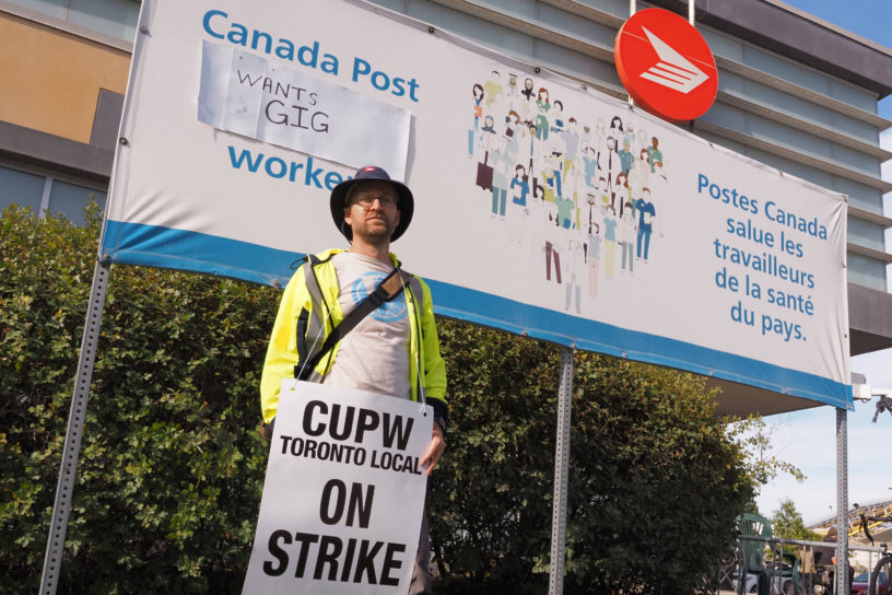 Image of a person holding a sign in front of a Canada Post building.