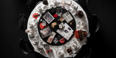 Image of a circular table with white bowls, plates and cups surrounding papers, picture frames and smaller items in the middle.
