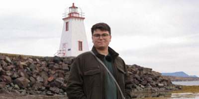 Image of Daniel Opasinis looking at the camera with a lighthouse in the background.