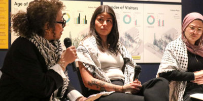 Image of three people sitting on a blue couch talking into microphones.