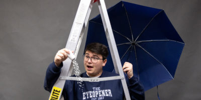 Image of a person under a ladder looking at a salt shaker that has salt pouring out of it while holding a blue umbrella.