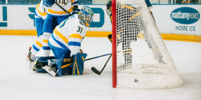 A Waterloo Warriors women's hockey player scoring on the TMU Bold women's hockey team sneaking a goal behind the goalie at the Mattamy Athletics Centre