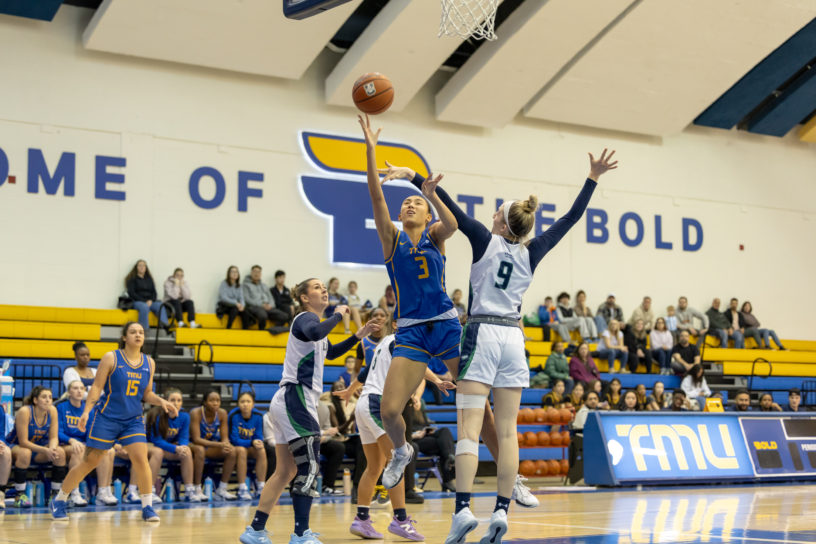 A TMU player reaches for the basket amidst Nipissing defense