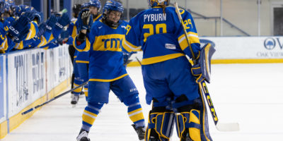 Two TMU Bold women's hockey players reaching for a high five in front on the TMU bench at the Mattamy Athletics Centre
