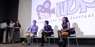 Image of three people sitting in front of a projector that reads "new voices film festival".