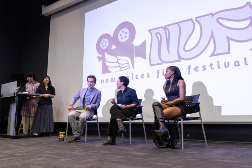 Image of three people sitting in front of a projector that reads "new voices film festival".
