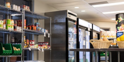 Image of a room with cans of food on the shelves and four fridges along the wall.