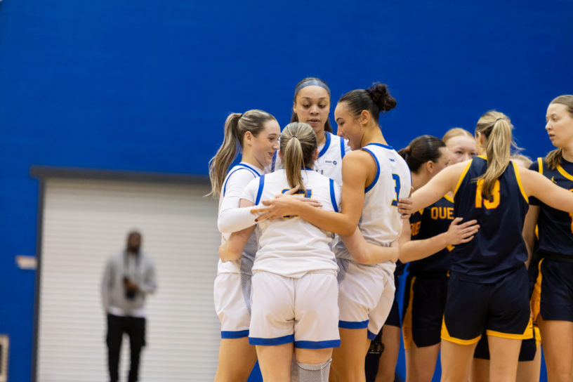 TMU women's basketball group together in a hug on the Mattamy Athletic Centre court